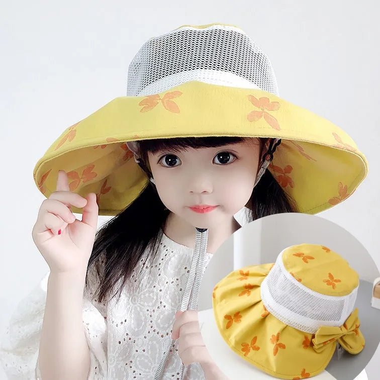 Child wearing a yellow sun hat with floral patterns, holding it up with one hand.