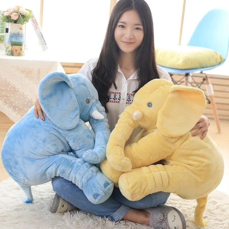 Woman holding a blue and a yellow elephant plush toy in a room.
