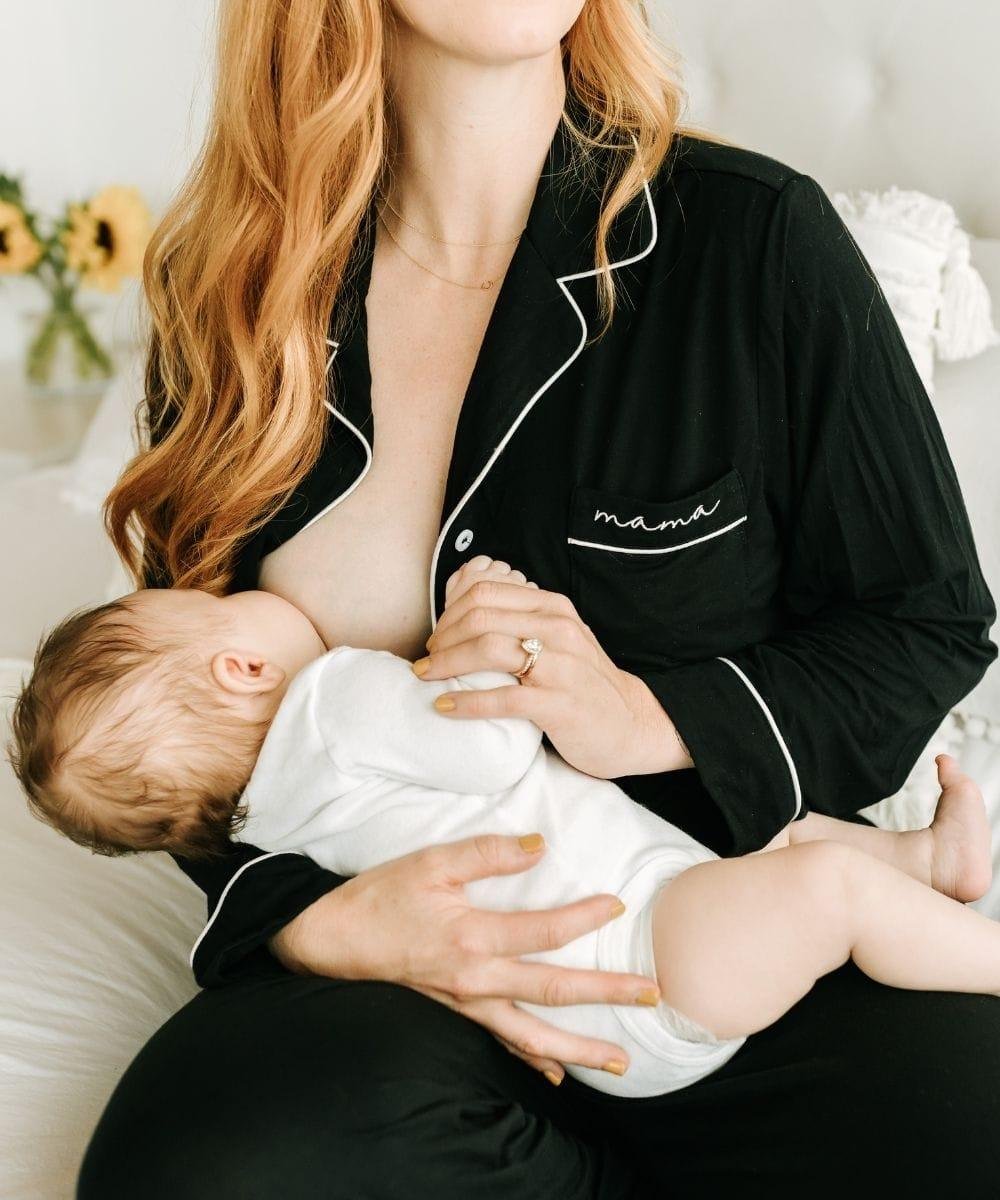 Woman in black pajamas with 'mama' on them, breastfeeding a baby.