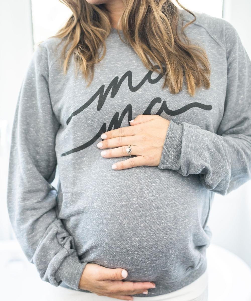 A gray sweatshirt with 'mom' printed on it, worn by a person holding their belly.