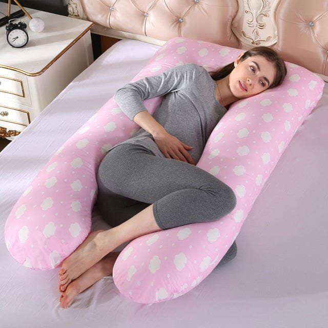 Woman lying on a pink polka dot U-shaped body pillow in a bedroom setting.