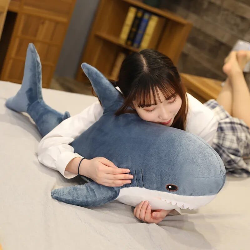 Person lying on a bed with a large shark-shaped pillow