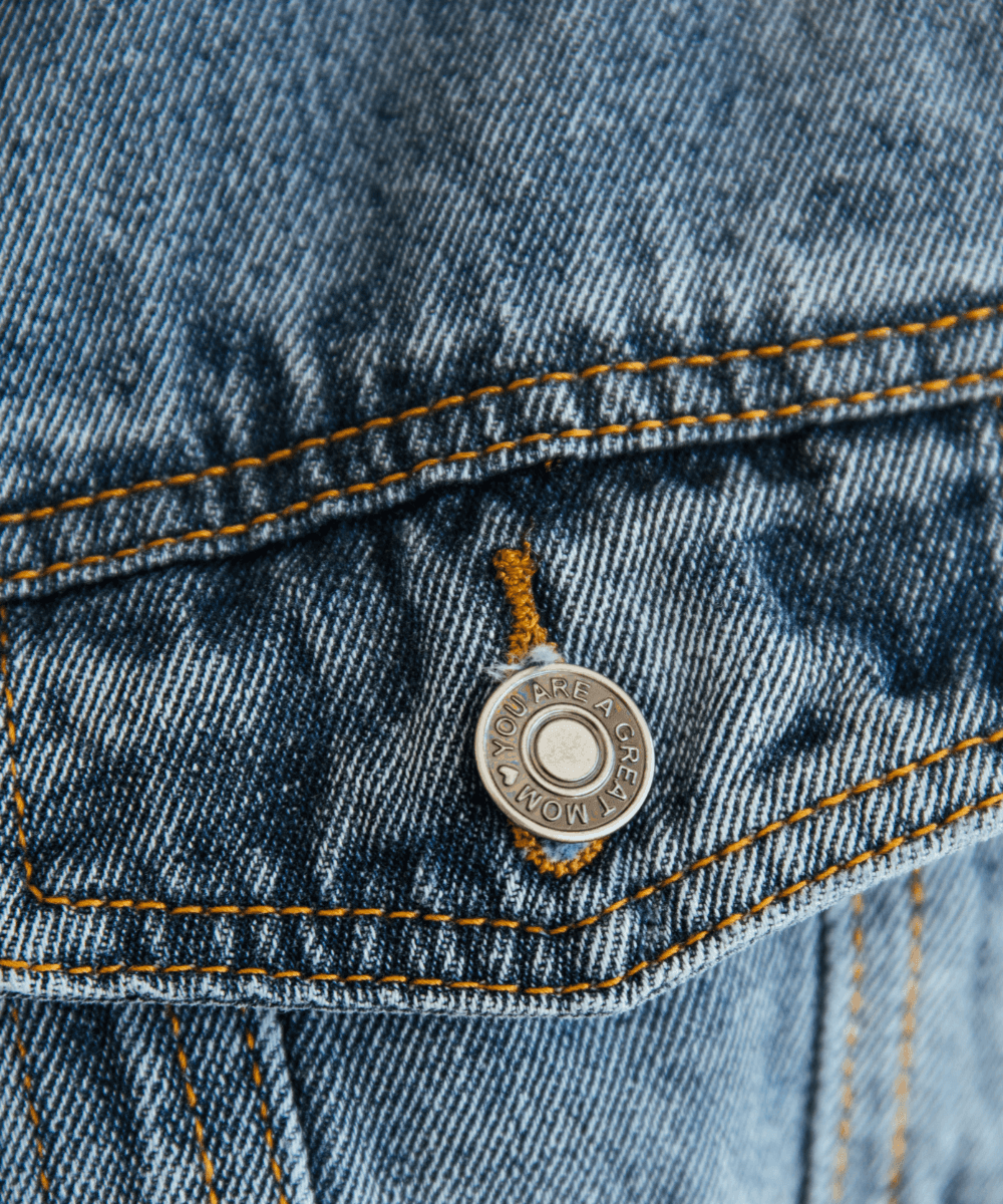 Close-up of a button on a denim jacket with a brand logo.