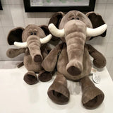 Two plush elephant toys on a white surface with a tiled wall background.