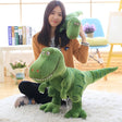 Woman holding a large green dinosaur plush toy in a room with books and a chair.