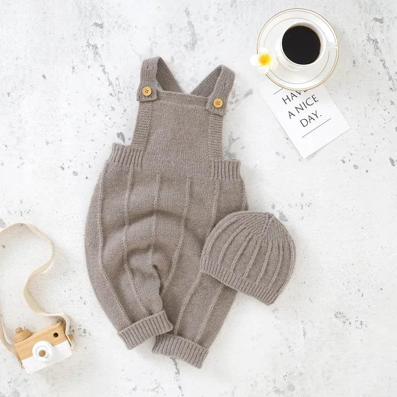 Knitted baby romper and hat set on a textured surface with a coffee cup and card.