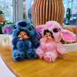 Two plush toys, one blue and one pink, sitting on a wooden table.