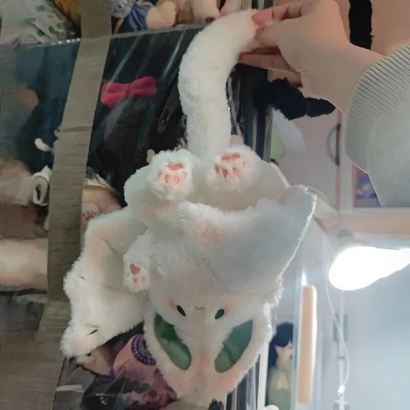 Plush toy with bunny ears held by a hand in front of a store display.