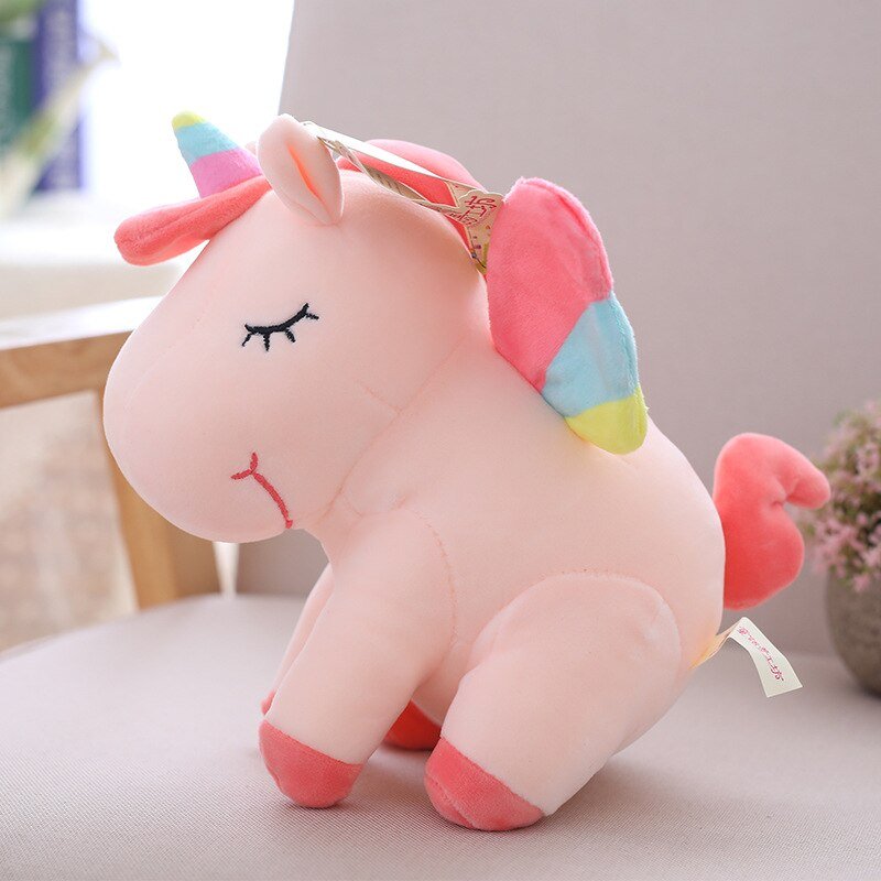 Pink unicorn plush toy with a rainbow horn on a light surface.