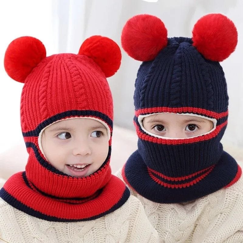 Two children wearing red and navy knitted hats with pom-poms on a white background.