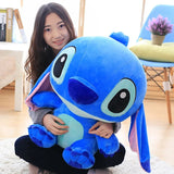 Person holding a large blue plush toy in a room with a chair and plant in the background