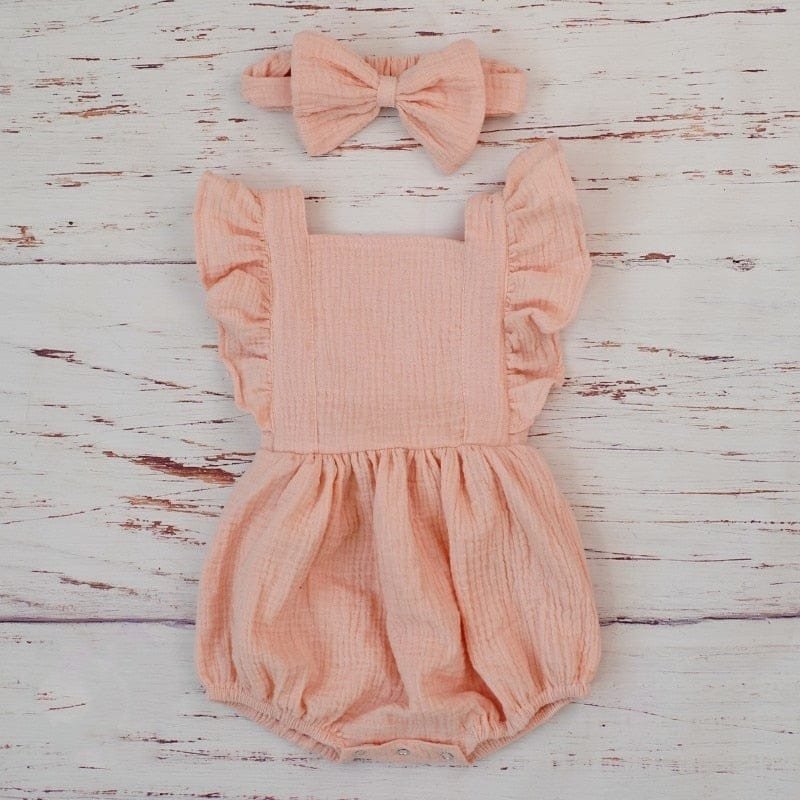 Pink baby romper with ruffled straps and matching headband on a wooden surface