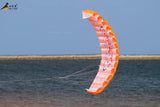 Orange and pink parafoil kite flying over a body of water with a clear blue sky.