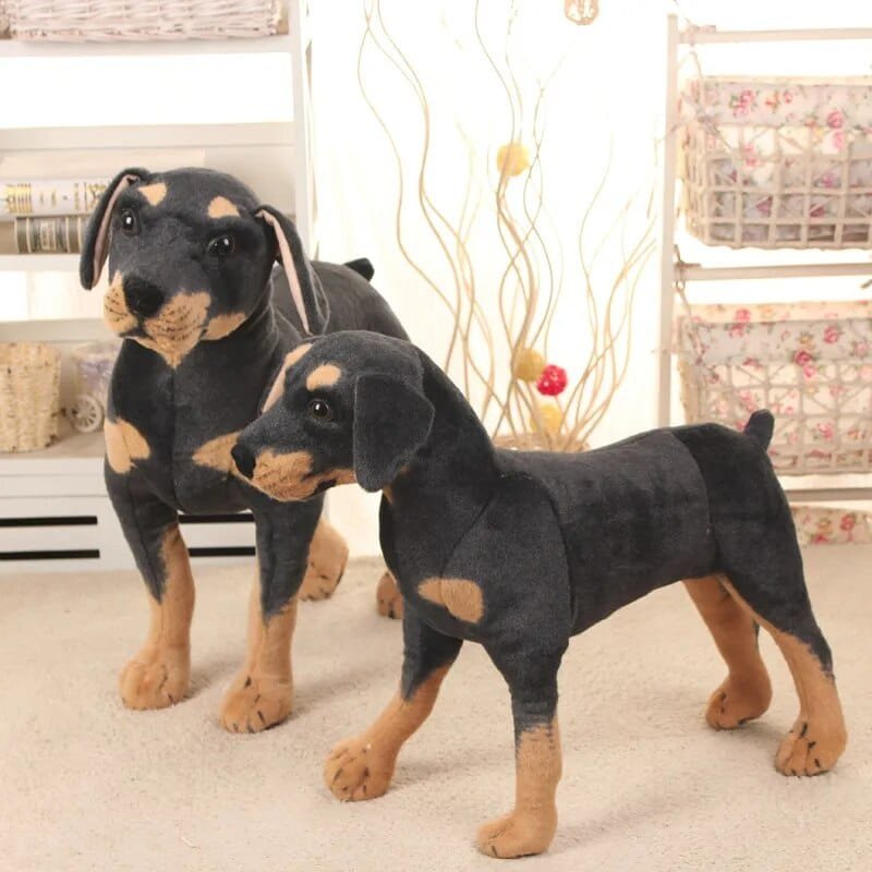 Two Doberman pinscher plush toys standing on a carpeted floor.