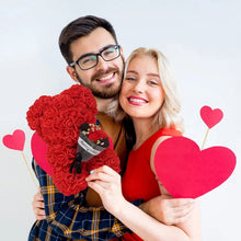 Couple holding heart props alongside the Rose Bear gift box, a romantic present idea for engagements and anniversaries.