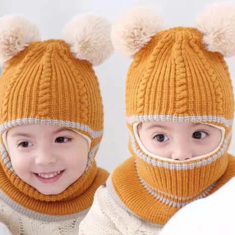 Two children wearing mustard yellow knitted hats with pom-poms and scarves on a white background.