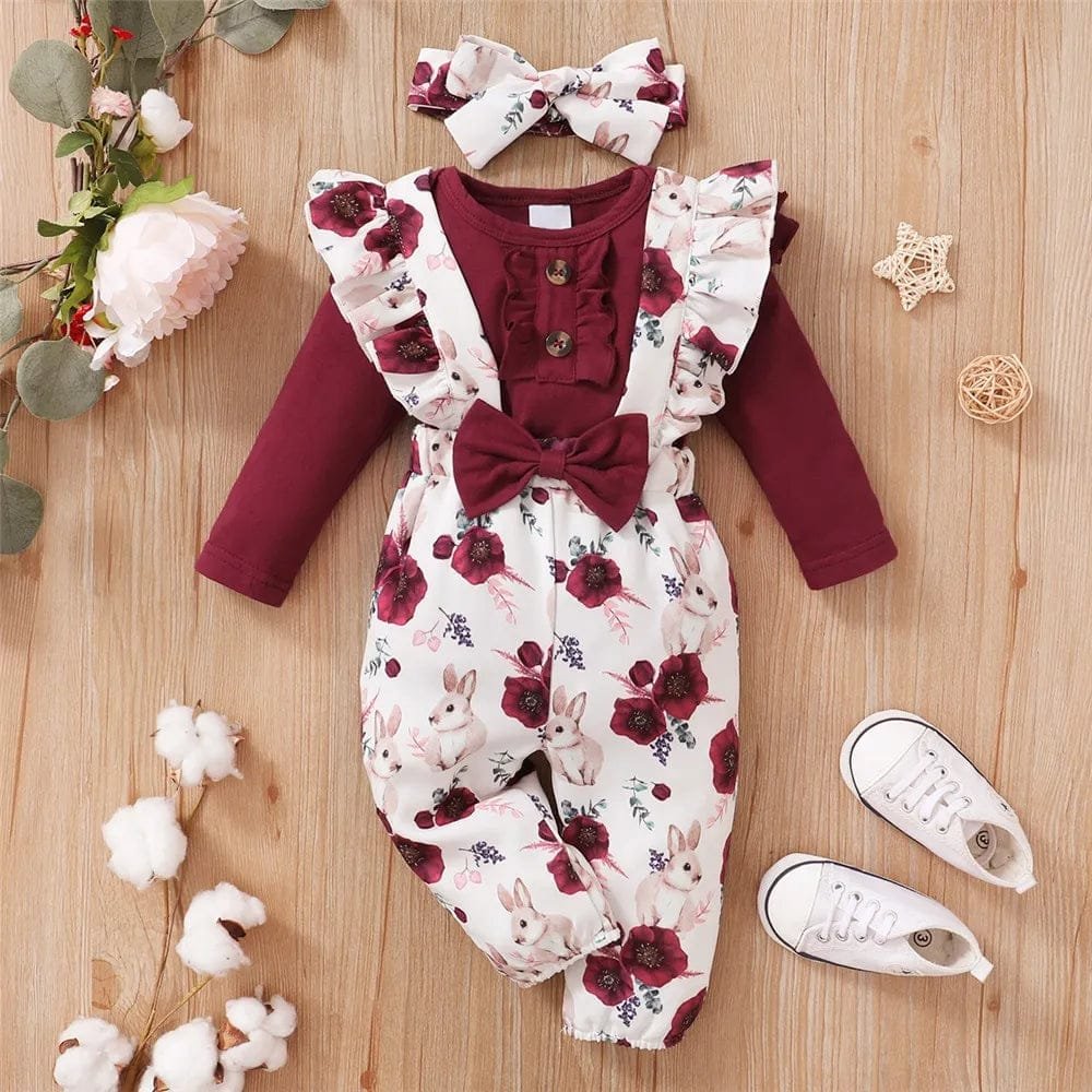 Baby romper with floral and bunny print on a wooden surface with shoes and decorative items.