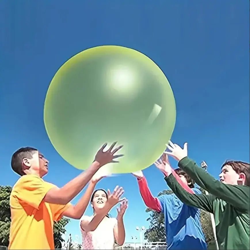 Children playing with a large green ball outdoors on a clear day