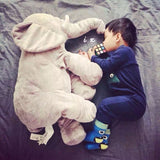 Child lying next to a large plush elephant toy on a bed