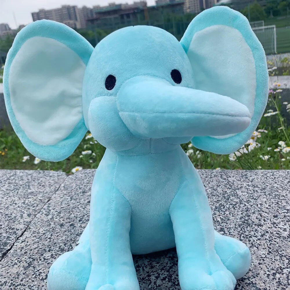 Blue elephant plush toy sitting on a concrete surface with grass and flowers in the background