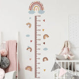 Children's growth chart with rainbow and cloud design on a white wall in a nursery.