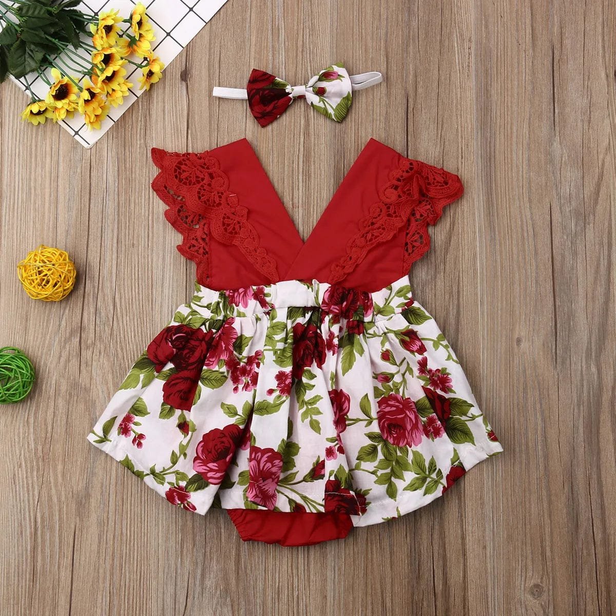 Red floral baby romper with matching headband on a wooden surface