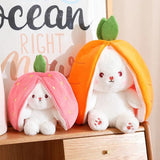 Two plush toys resembling bunnies inside fruit-shaped houses on a wooden surface.