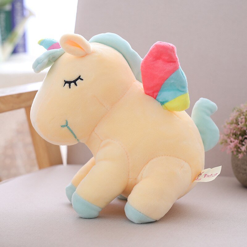 Plush unicorn toy with rainbow-colored wings on a light surface.