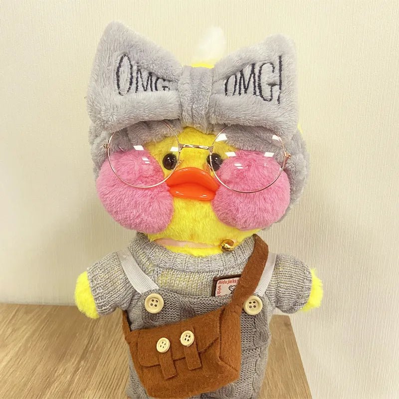 Plush toy with a yellow face, gray bow, and pink cheeks on a wooden surface.