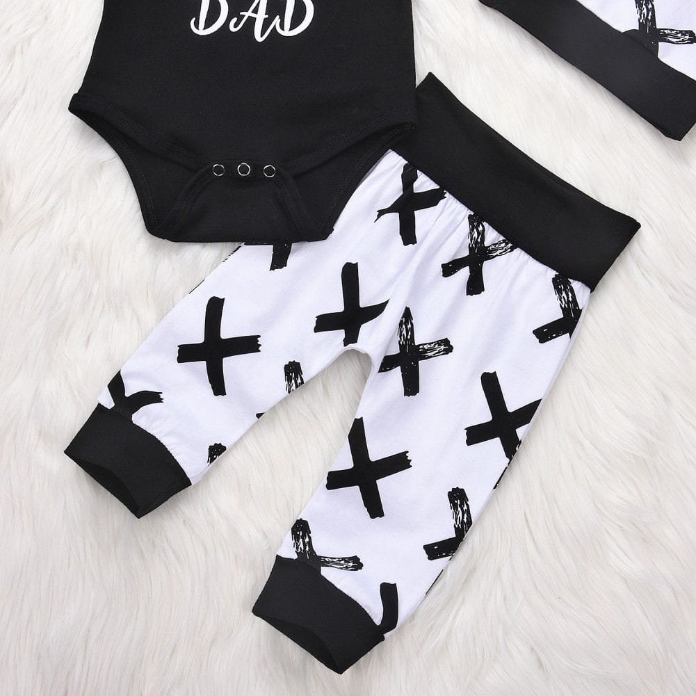 Black and white baby outfit with 'DAD' text on a light wooden surface