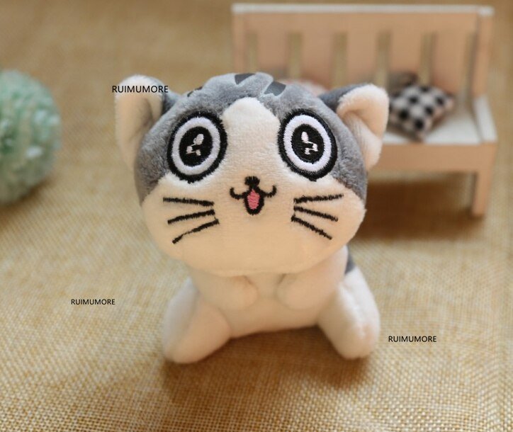 Plush toy cat with large eyes on a textured surface, brand 'RUMUMORE' visible.
