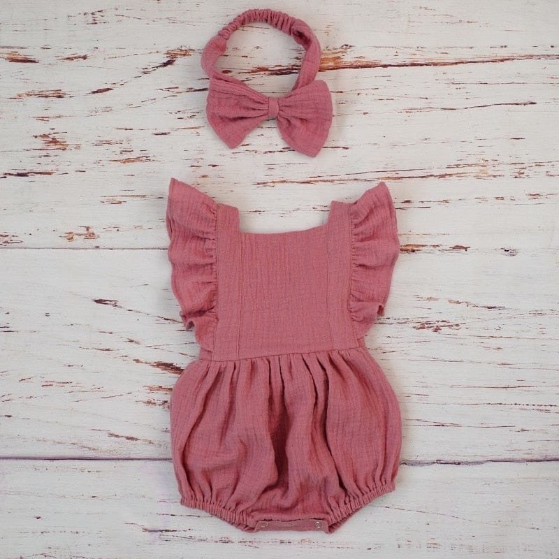 Pink baby romper with ruffles and matching headband on a wooden surface