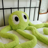 Green plush octopus toy on a bed with a black metal headboard.