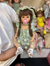 Doll with a pacifier held by a person, surrounded by other dolls in the background.