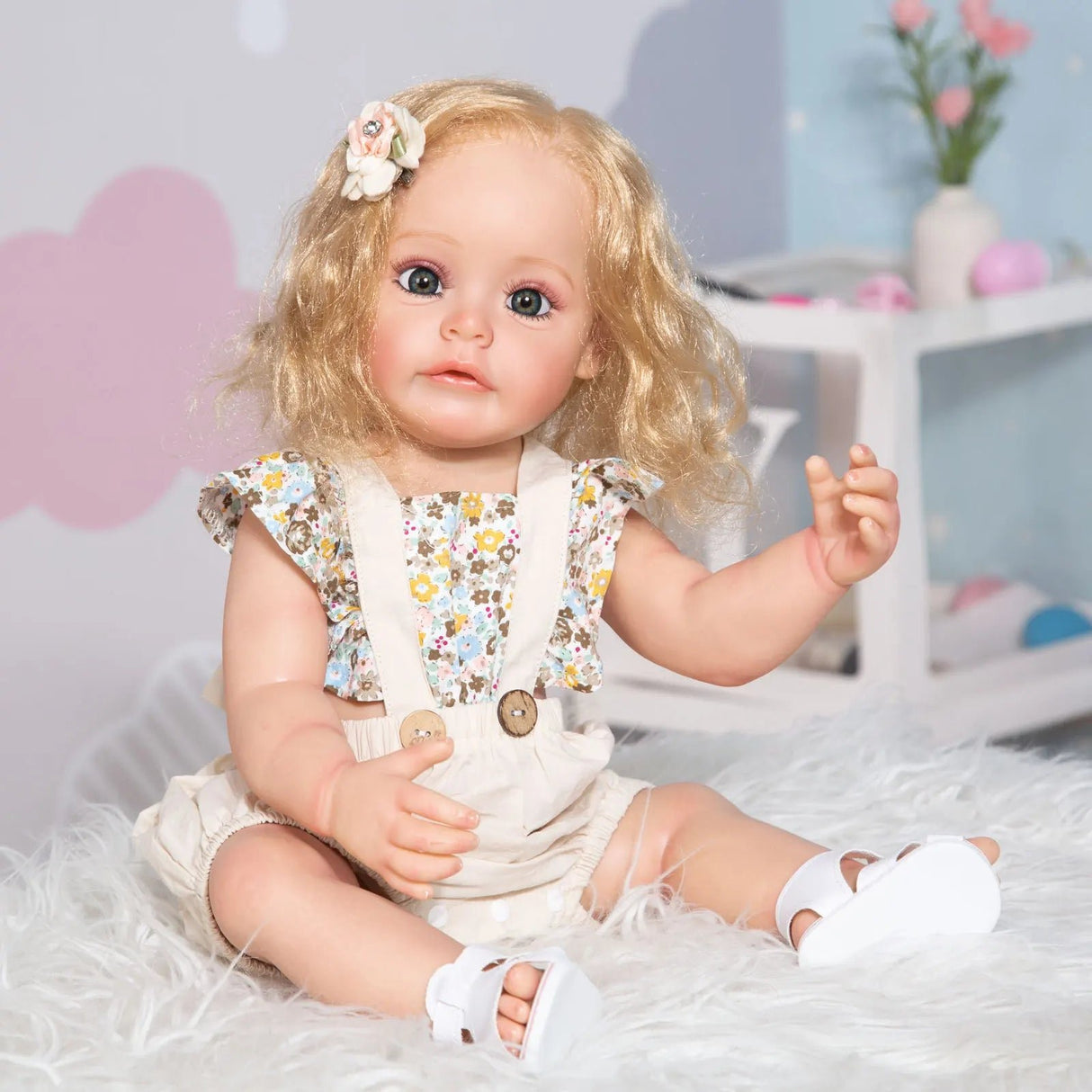 Realistic baby doll with blonde hair and floral dress sitting on a soft surface.