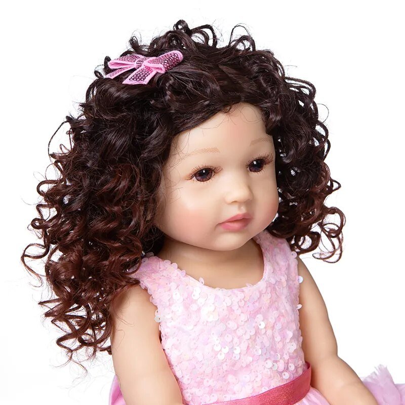 Silicone Reborn Toddler Doll with curly brown hair and pink outfit, a soft touch fashion doll for cuddling and keepsake collecting.
