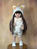 Real-feel Standing Reborn Doll in a bear-ear knit set on a wooden stand, a soft silicone doll for display and pretend care.