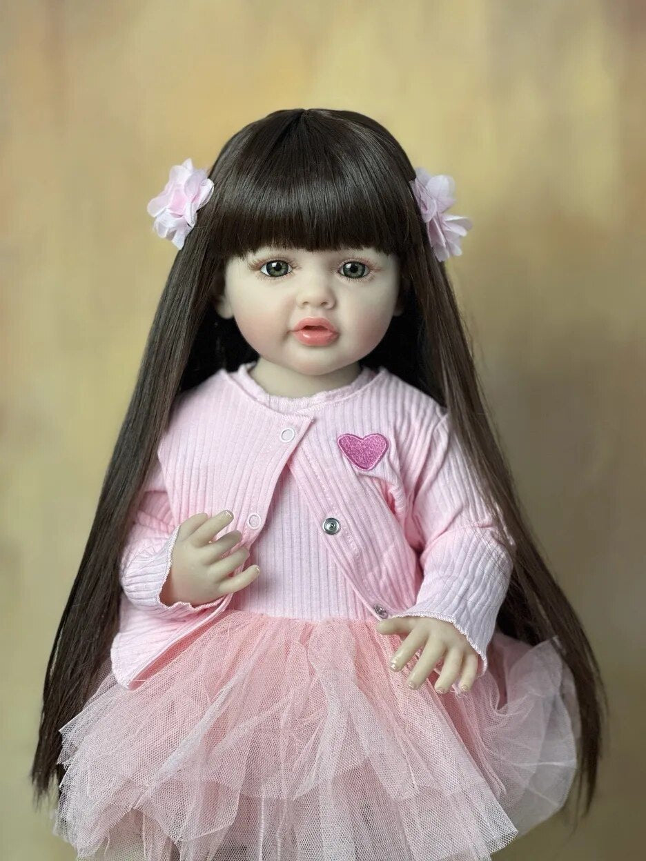 Standing Reborn Doll with long brown hair in a pink dress and cardigan, a silicone baby doll for role play and gift giving.