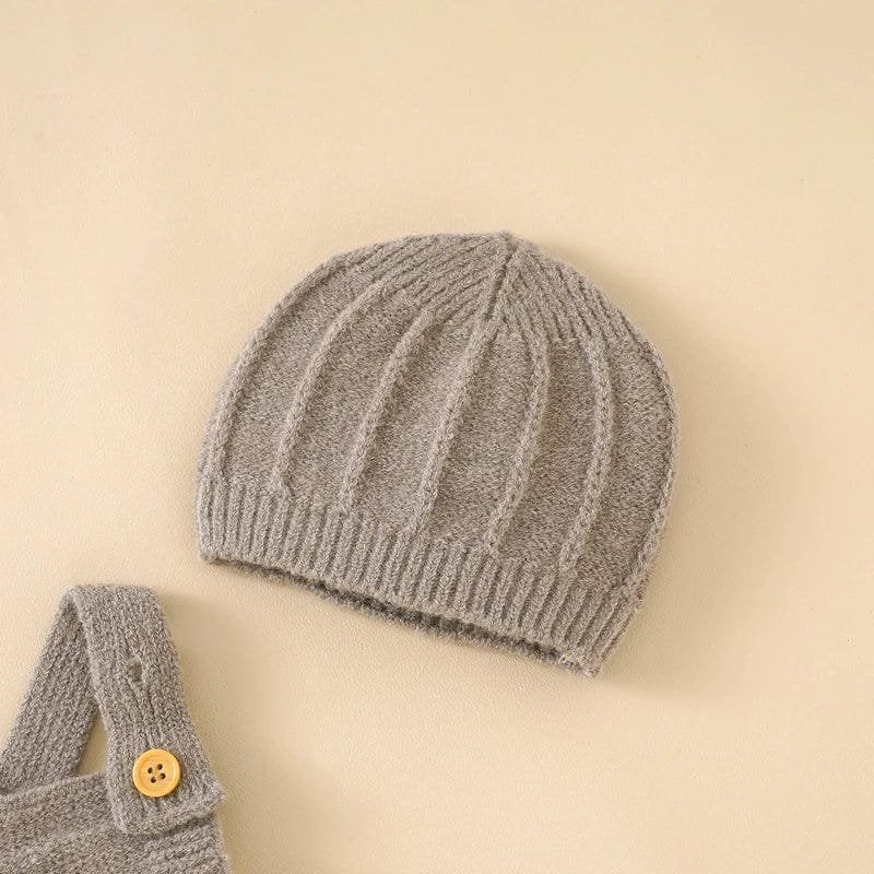 Gray knit baby hat and matching romper with a button on a beige background