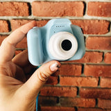 Hand holding a small blue camera against a brick wall