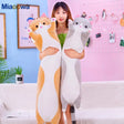 Person holding two large plush toys resembling a fox and a raccoon in a room with a pink wall and plants.