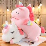 Two pink and white unicorn plush toys on a wooden surface with a softly blurred background.