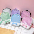 Set of clear backpacks with colorful bows on a tiled surface and pink wall background