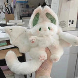 Plush toy resembling a white creature with large ears held in a hand, office background