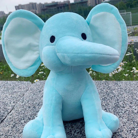 Blue elephant plush toy sitting on a concrete surface with grass and flowers in the background