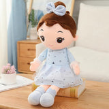 Plush toy girl doll with brown hair and a blue dress on a wooden surface.