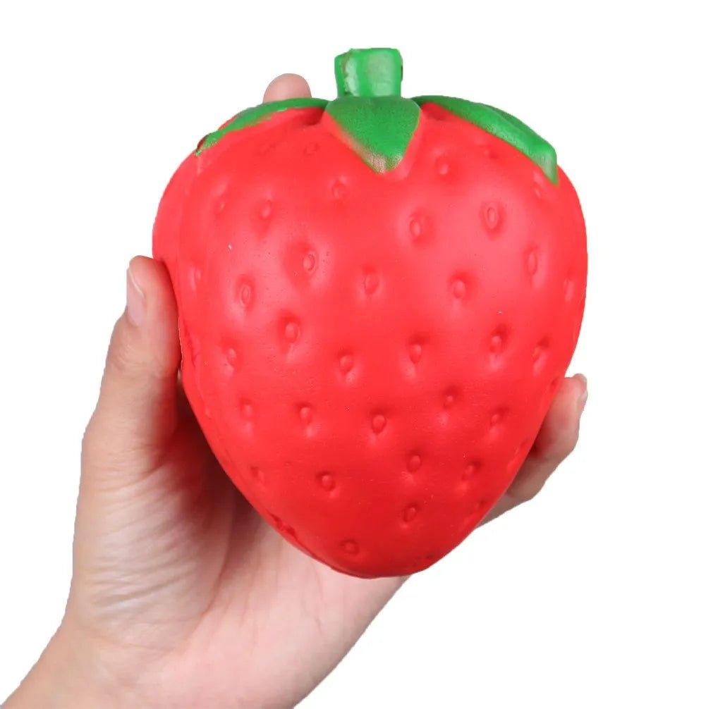 Hand holding a strawberry-shaped squishy toy against a white background