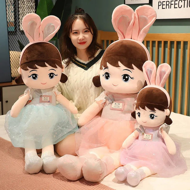 Three plush toys with bunny ears and dresses on a bed