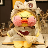 Plush toy duck wearing glasses, a sweater, and a bow hat on a decorative surface.