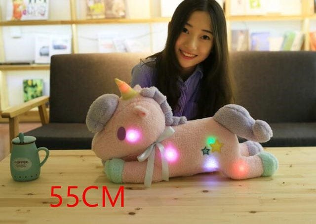 Woman sitting behind a glowing unicorn plush toy on a table.